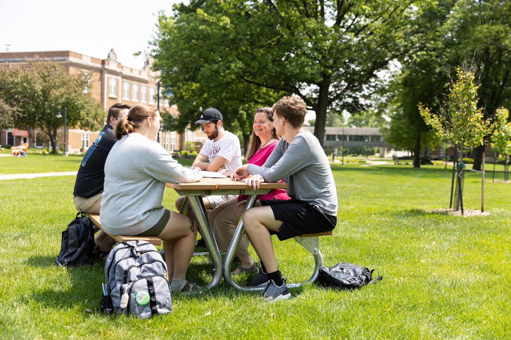 Students and professor sitting at a picnic table on the campus mall
