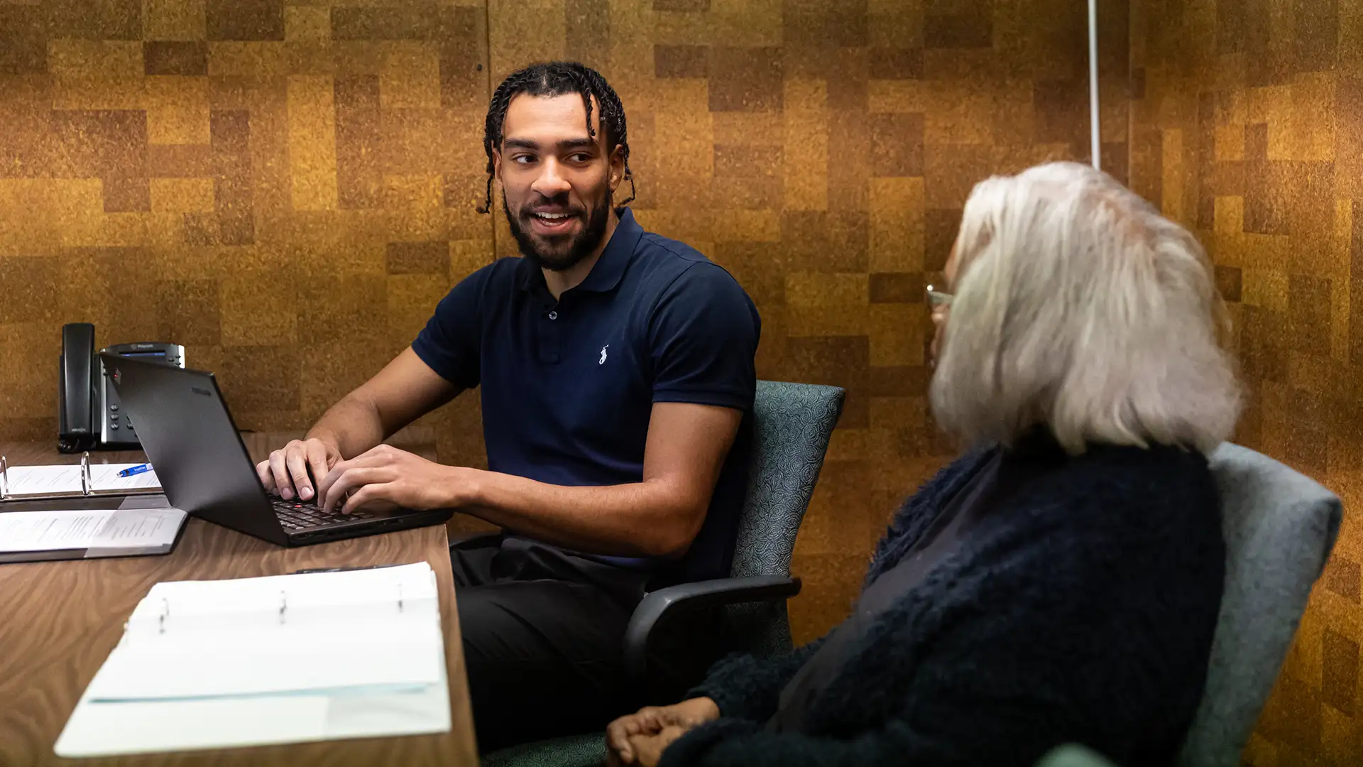 A young man faces the camera and is speaking to an older woman whose back is to the camera. 