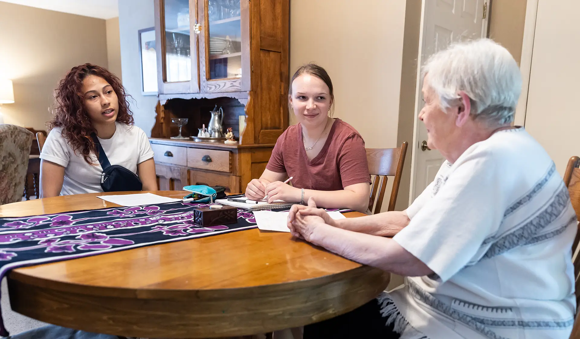 Students with an older woman having a conversation around a dinner table