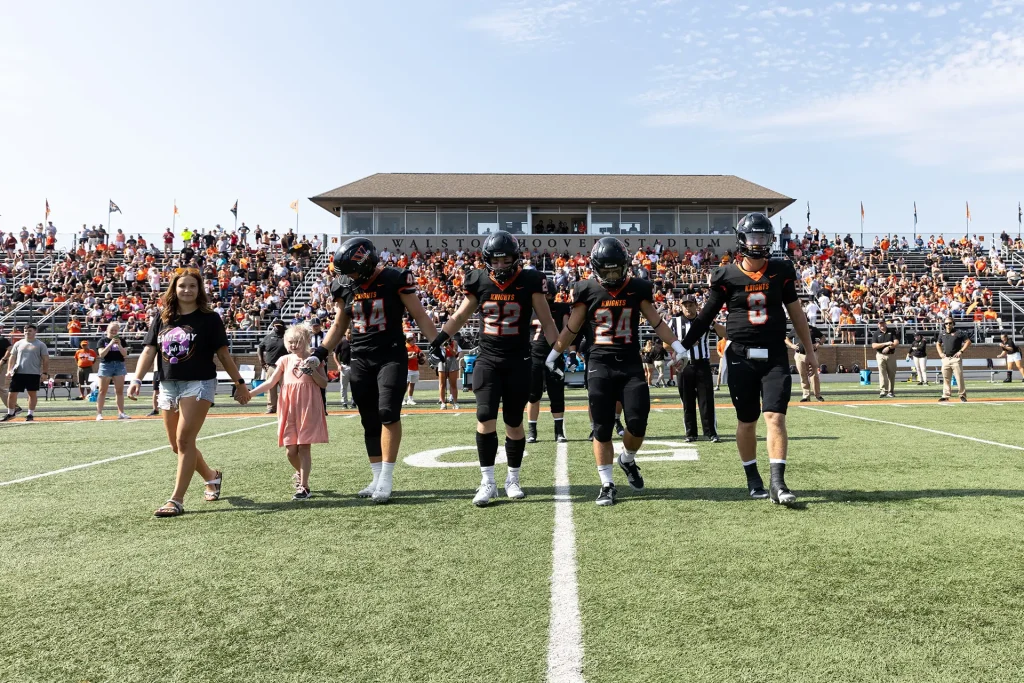 Football team captains walk out on field with kid captain