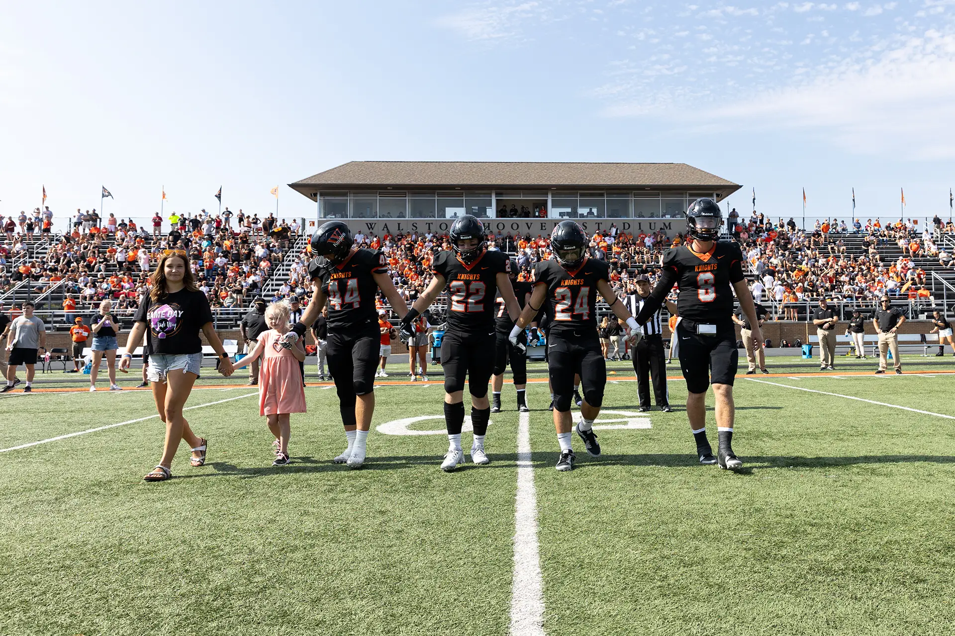 Football team captains walk out on field with kid captain