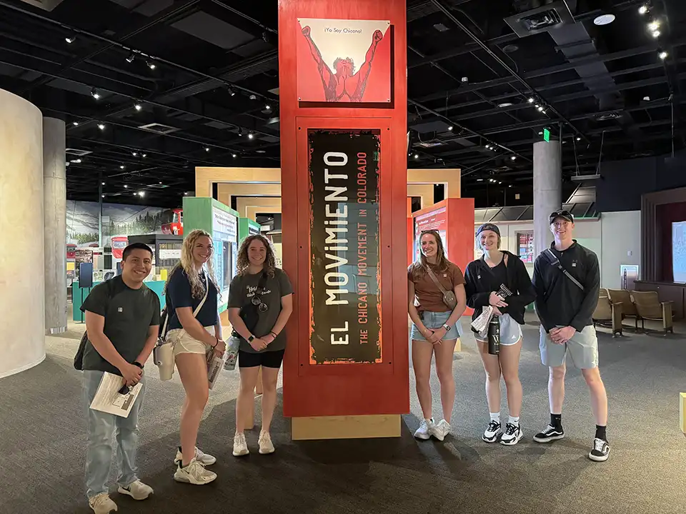 Students stand around a large red column that reads El Moviemento The Chicano Movement in colorado