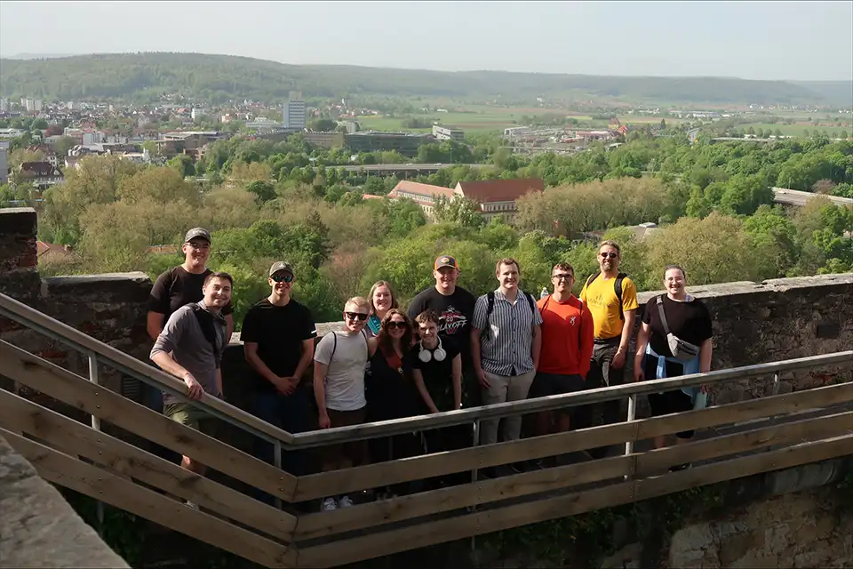 Students stand on a bridge walkway in Germany with a rural landscape behind them