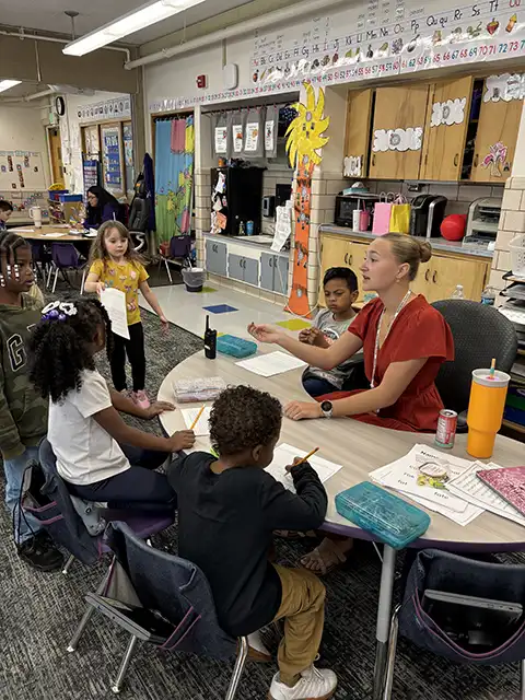Wartburg student sits behind a small table with several school-aged children sitting in front of her.