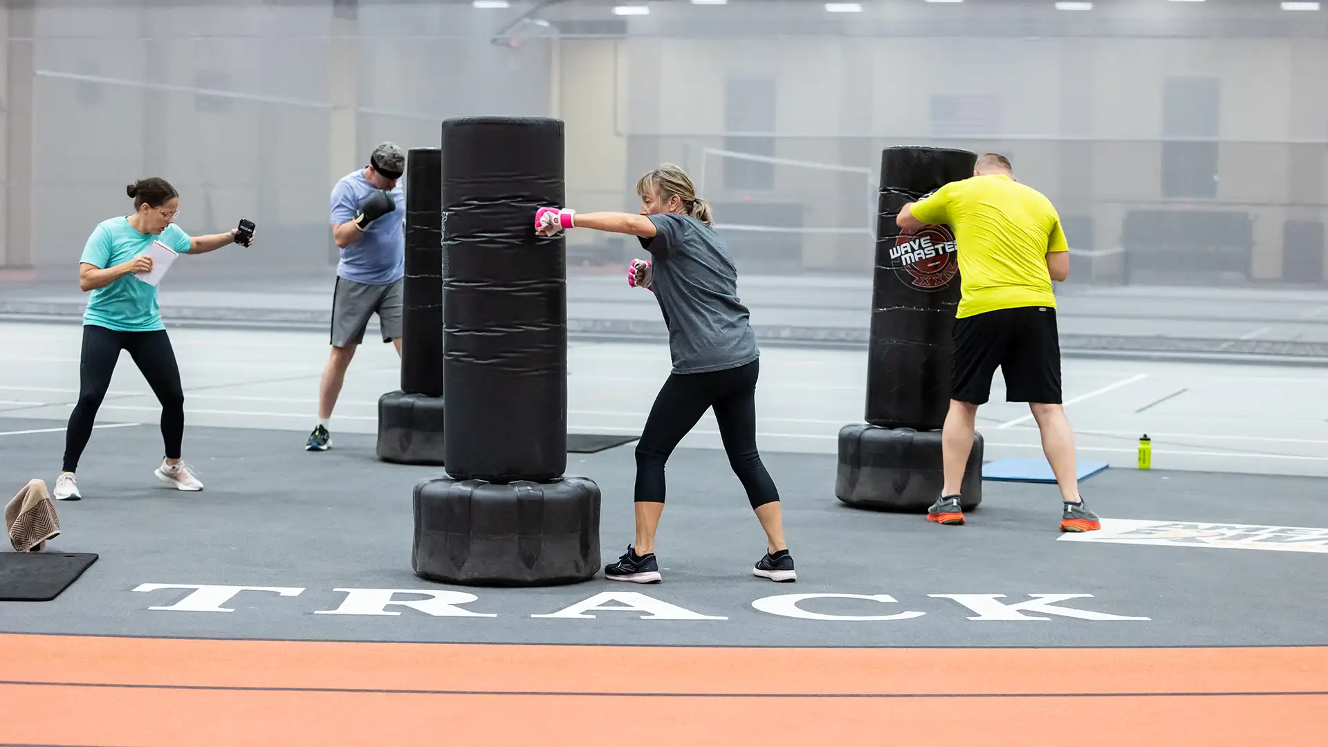 Three individuals participate in a kickboxing class while the instructor provides guidance.