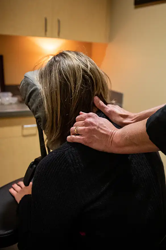 Hands massaging a person's neck while sitting in a massage chair.