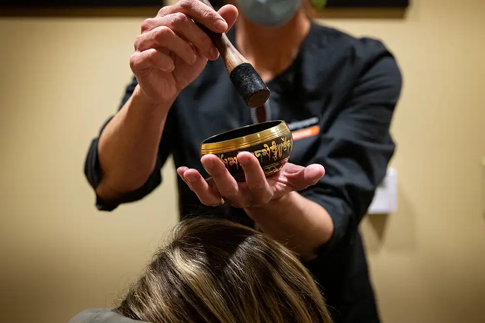 A therapist uses a singing bowl over a client's body during a massage.