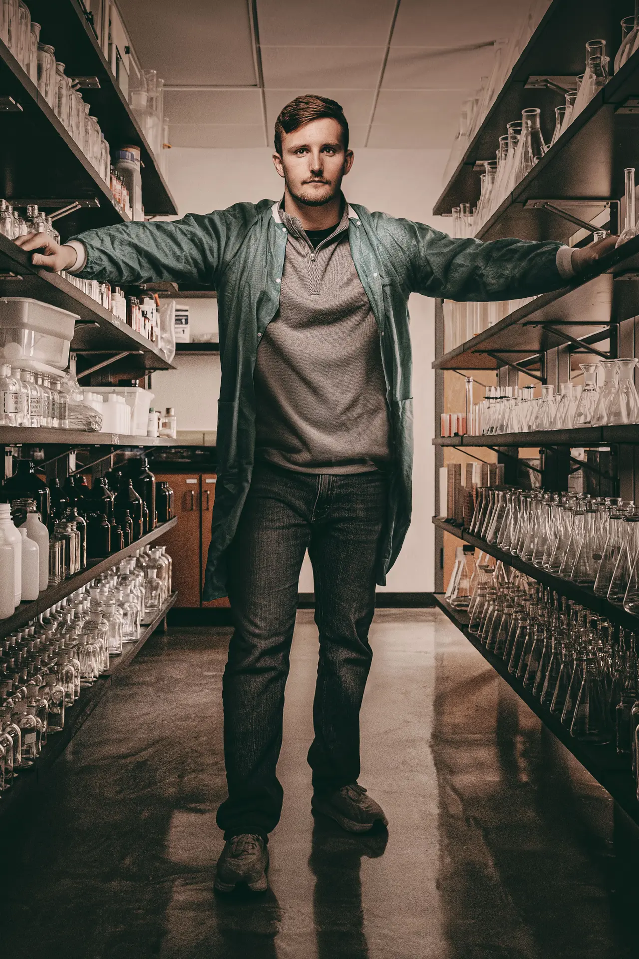 Owen Grover stands between two racks of shelving full of beakers and other science equipment.