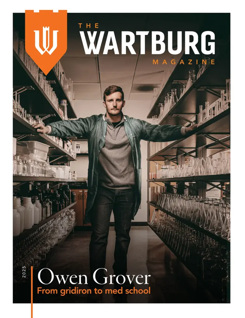 The cover of the 2025 edition of The Wartburg Magazine, featuring Owen Grover standing between two shelving units filled with beakers and other science equipment.
