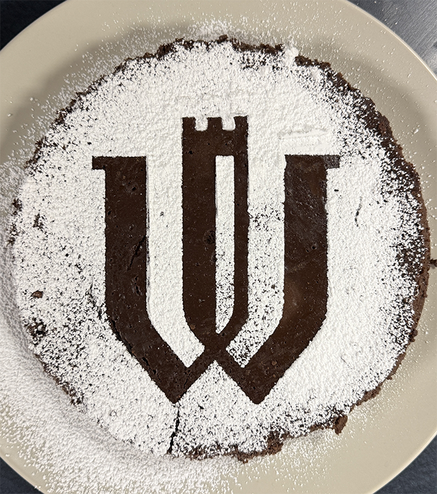 A round pan of brownies with a powdered sugar dusting that leaves the Wartburg monogram in negative.