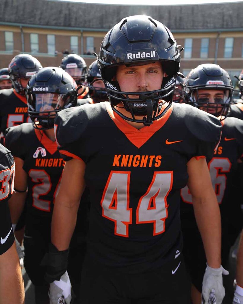 Owen Grover leads the football team onto the field before a game. He is wearing his helmet and #44 jersey. 