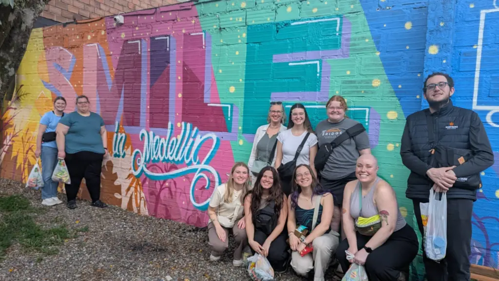 Student and staff pose in front of an brightly colored exterior wall in Colombia that reads Smile in Medillin 