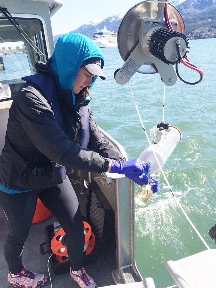 Hope O'Neill collects water samples over the side of a boat.
