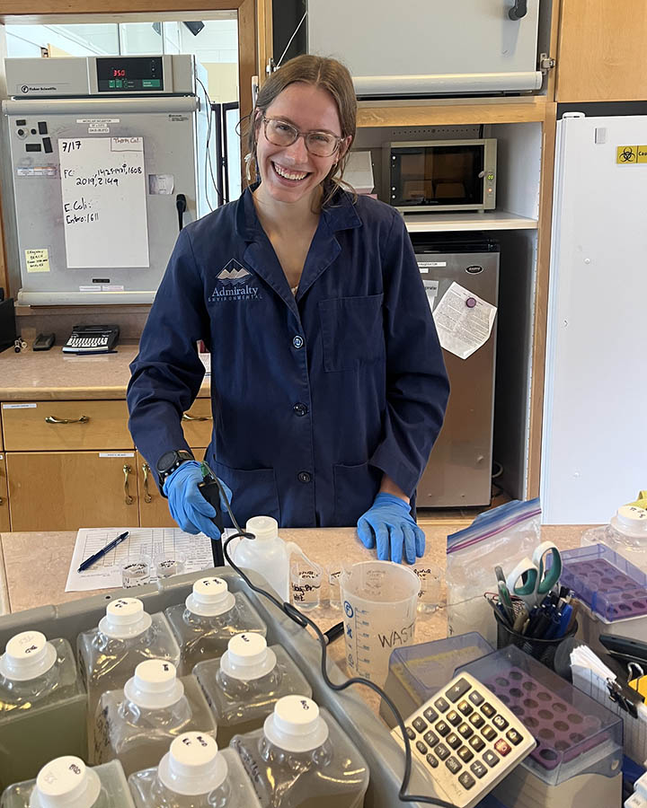 Leah Cherry stands behind a lab table in a navy blue Admiralty Environmental lab coat.