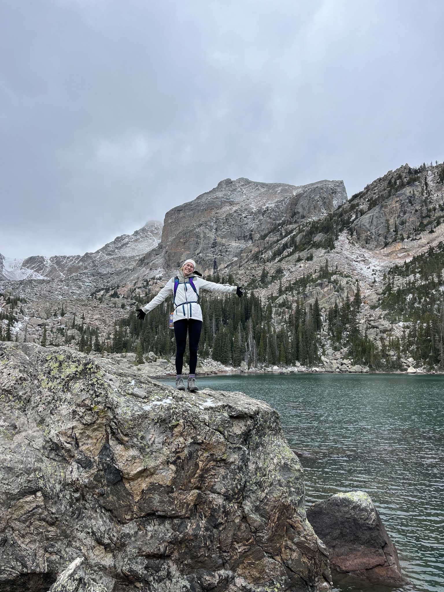Leah Cherry stands atop a cliff with her arms outstretched, a mountain in the background.