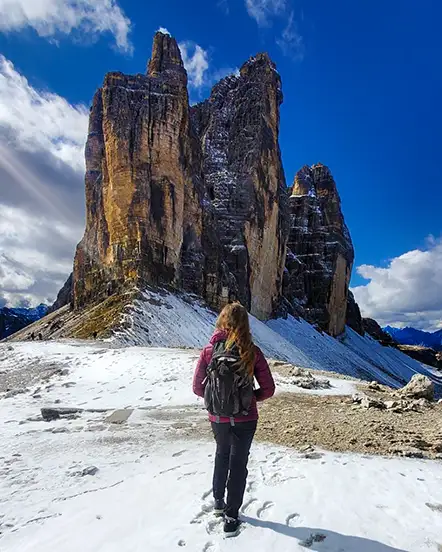 Natalie Bonthius stands on snowy ground facing a large rock cropping. Her back is to the camera. 