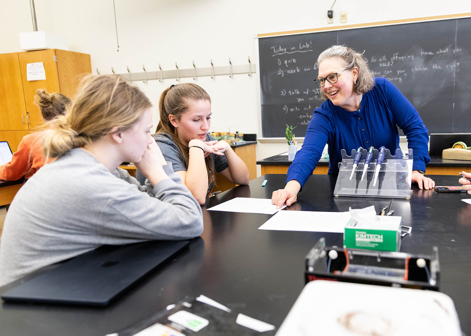 Stephanie Toering Peters leans over a lab table to help two female students.