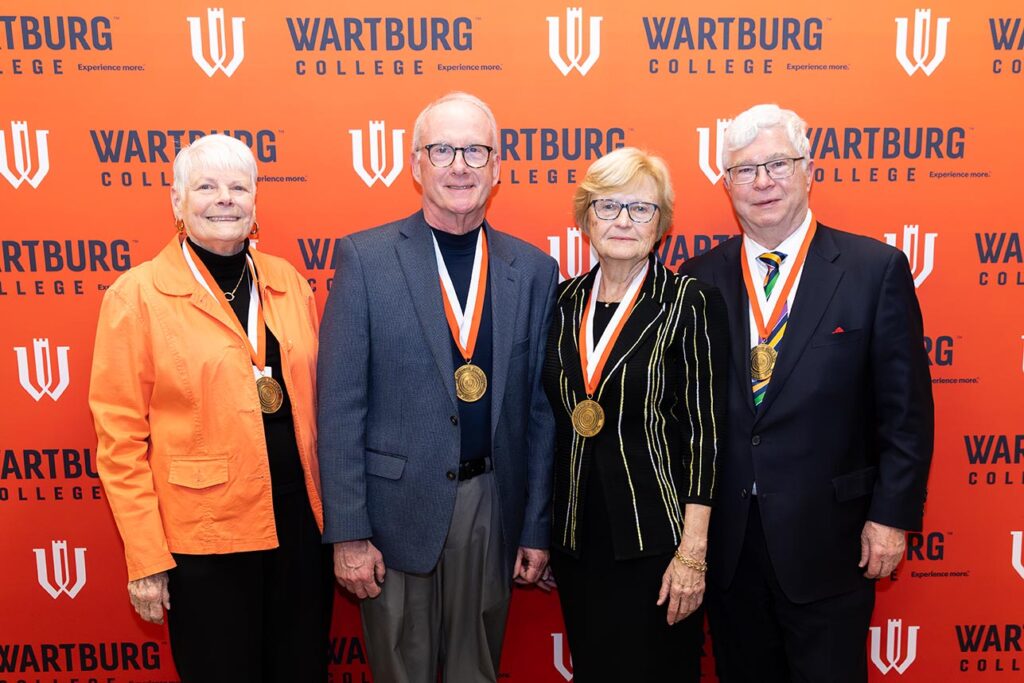 left to right Susan Vallem, the Rev. Michael Burk; Jane Noah and Steve Noah stand in front of an orange Wartburg College backdrop. All are wearing their Wartburg Medals around their neck. 