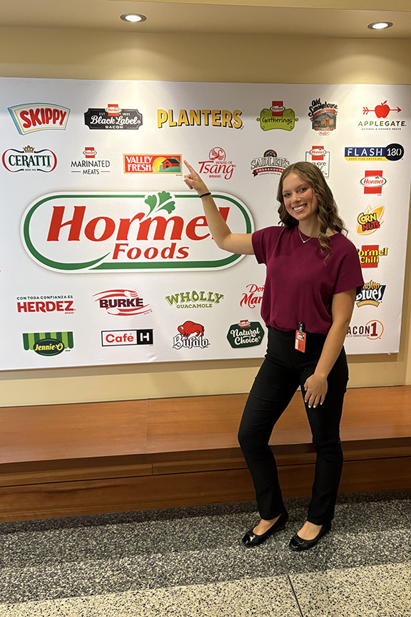 Nora Tweeten stands in front of a Hormel sign pointing to the brand she interned with.