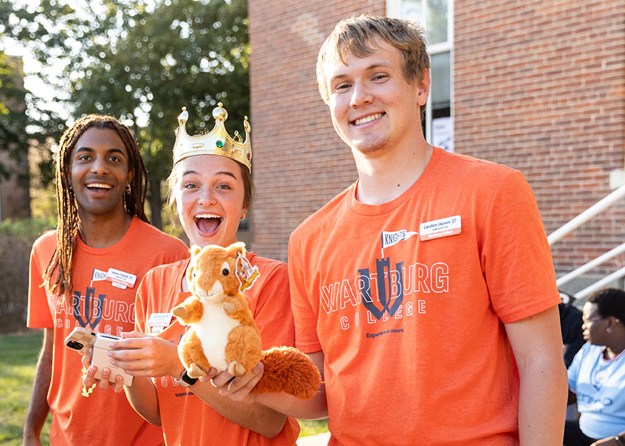 Erica Knupp stands between two men. One of the men is holding a stuffed squirrel and Erica has a fake crown on her head.