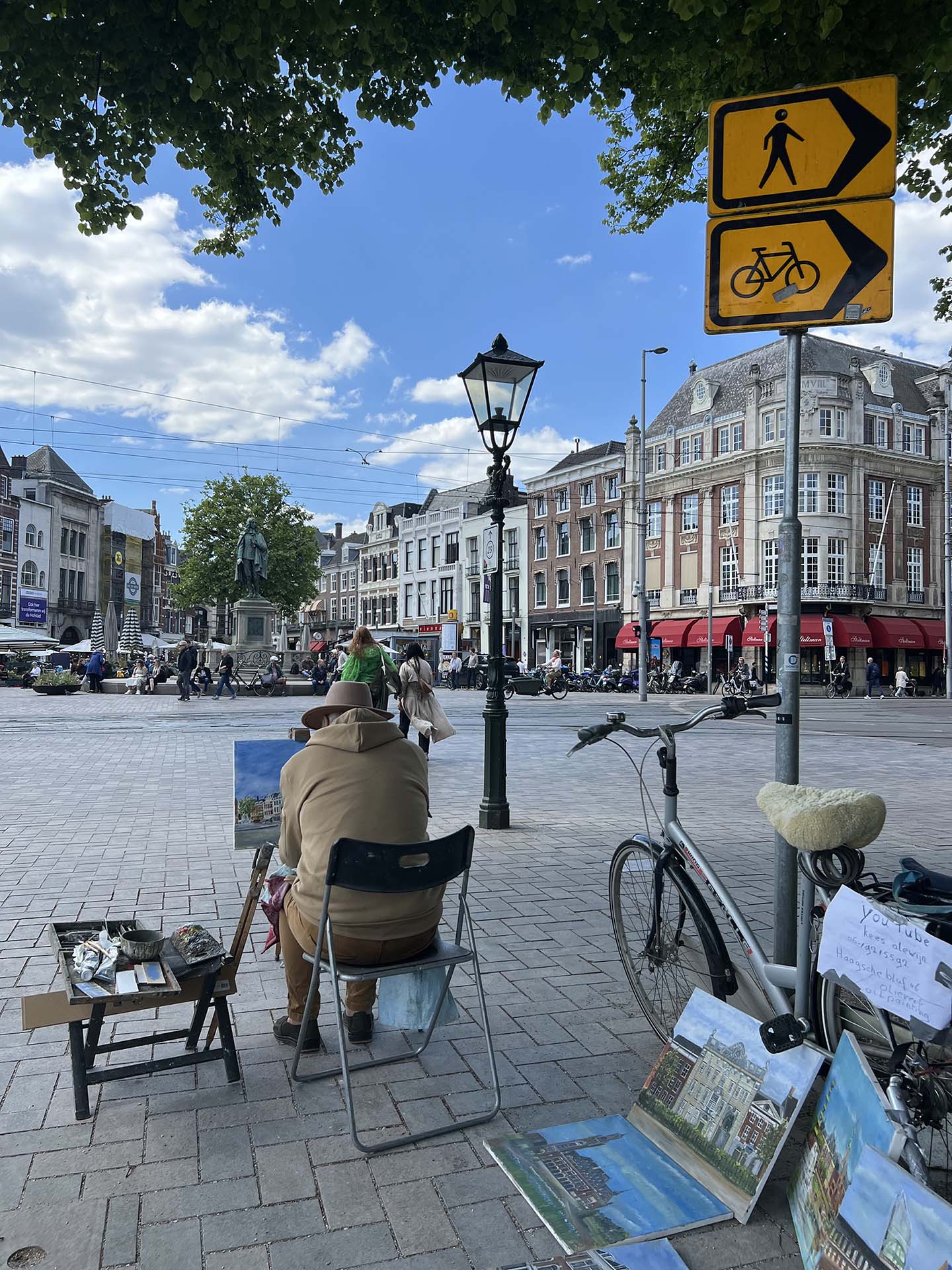 An unknown person sits with their back to the camera painting a picture on a Prague street.