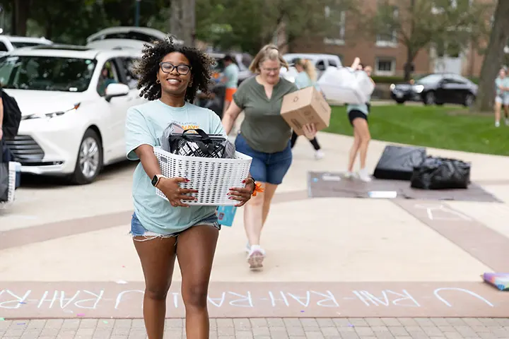 An Orientation leader carries a student's belongings to their residence hall on move-in day.