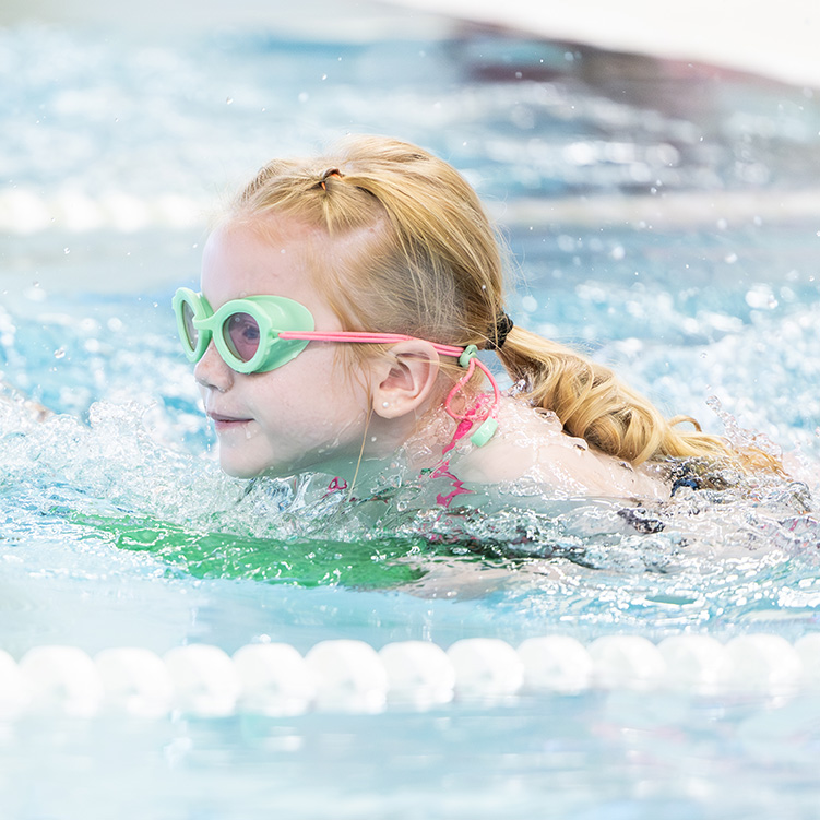 Young girl in goggles swimming with the help of a board.