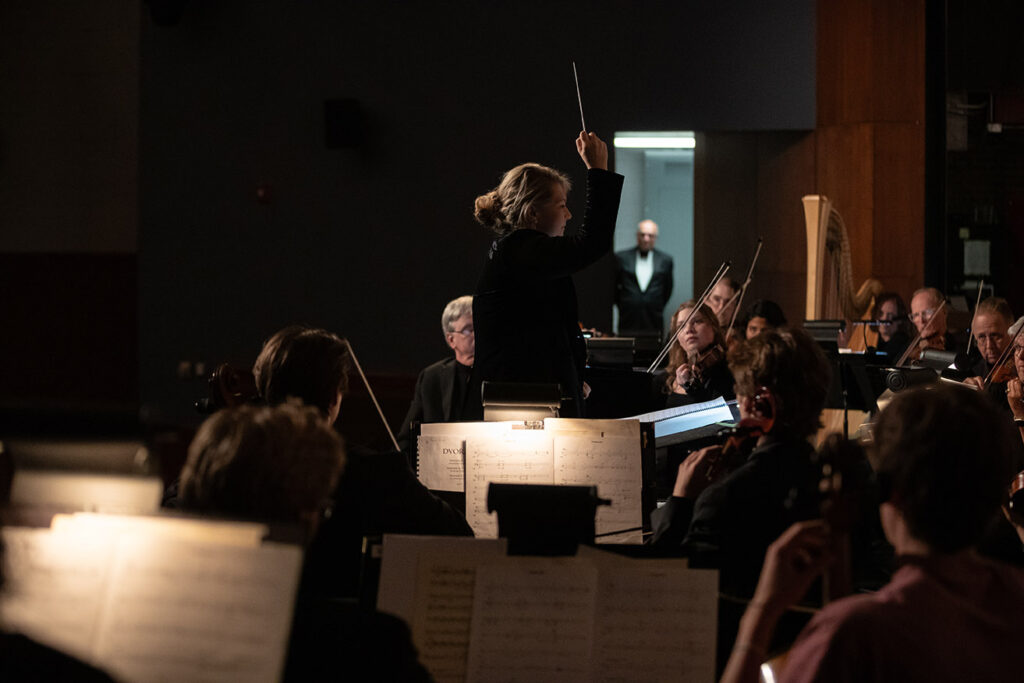 Rebecca Nederhiser conducts the Wartburg Community Symphony in the foreground. Jim Loveredge can be seen waiting in the wings in the background.