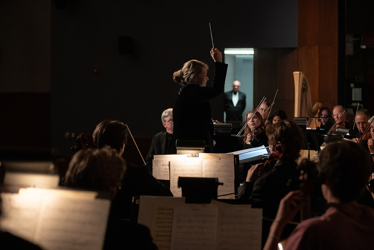 Rebecca Nederhiser conducts the Wartburg Community Symphony in the foreground. Jim Loveredge can be seen waiting in the wings in the background.
