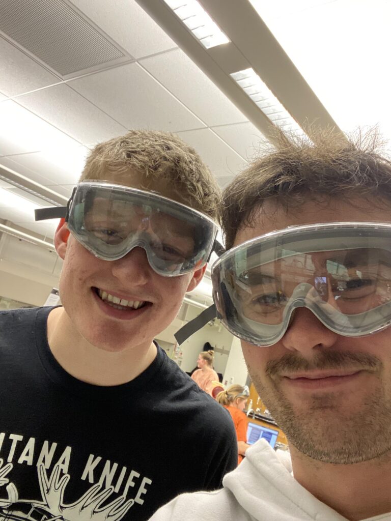 Jack Crane and his friend wearing goggles in a science lab.